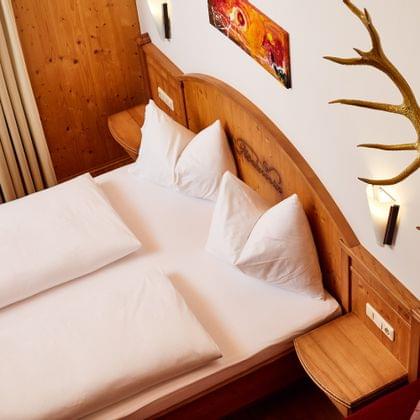 Cozy hotel room with double bed, wooden headboard, antler decor and modern wall lighting